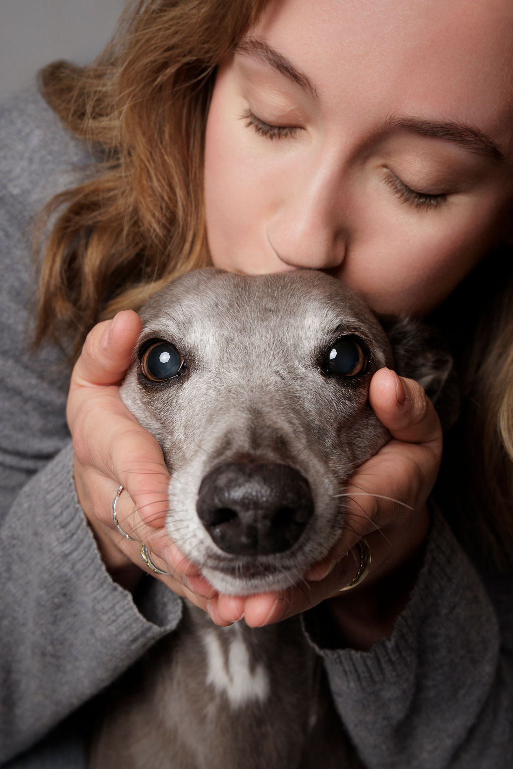A woman hugging a curly-coated doodle, her eyes closed